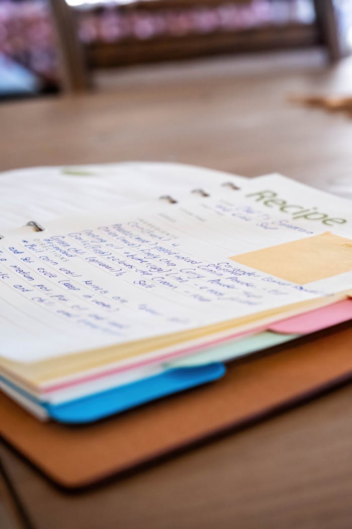 A detailed look at a handwritten recipe book with colorful dividers on a wooden table.