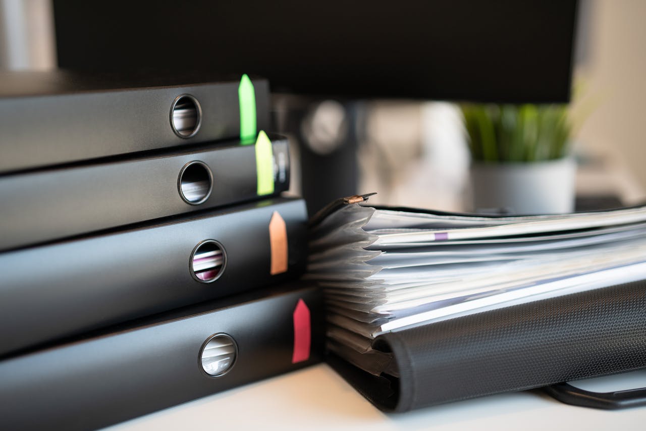 Stack of colorful ring binders and documents on a modern office desk setting.